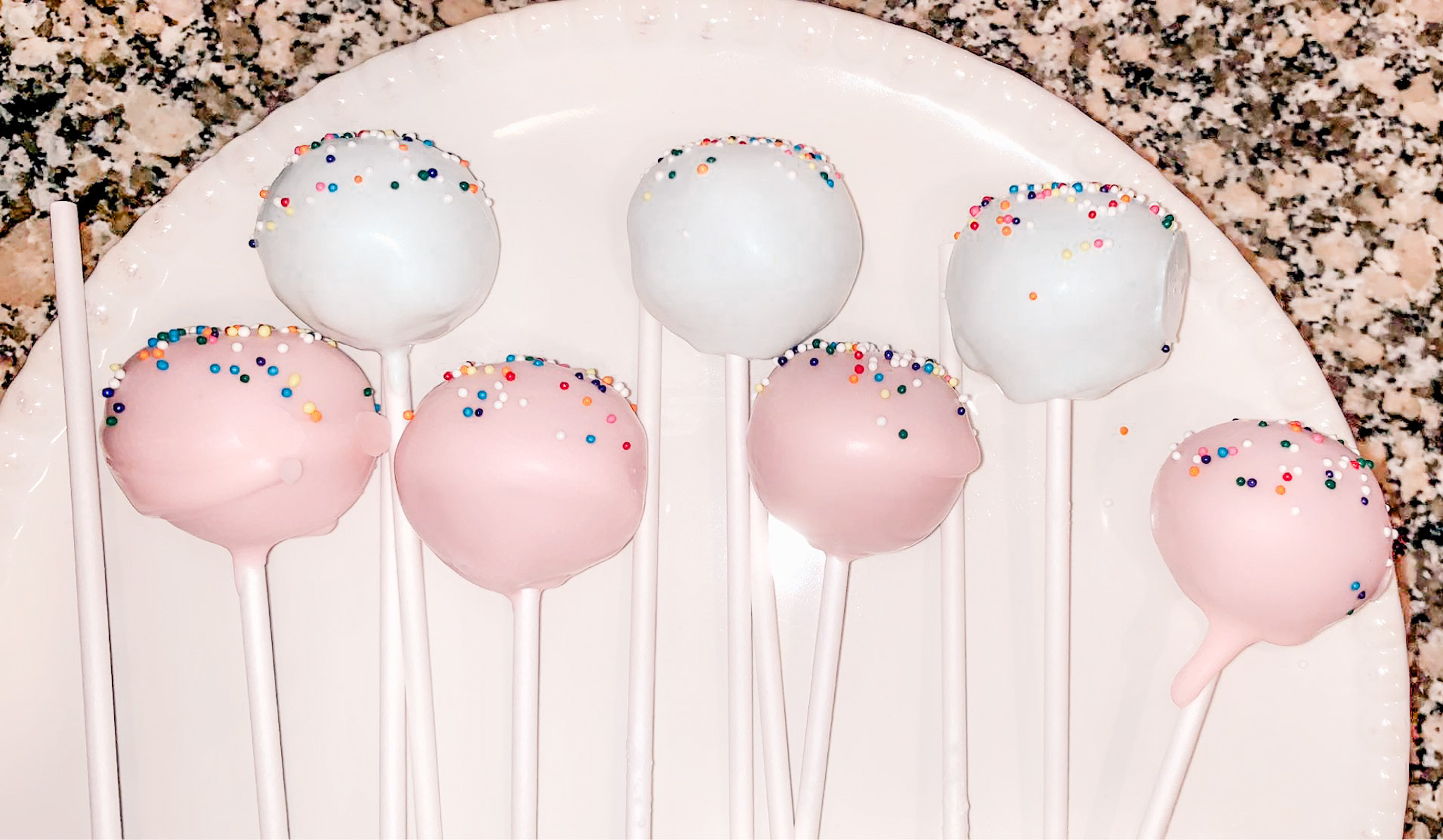 Light pink and blue cake pops with sprinkles on top.